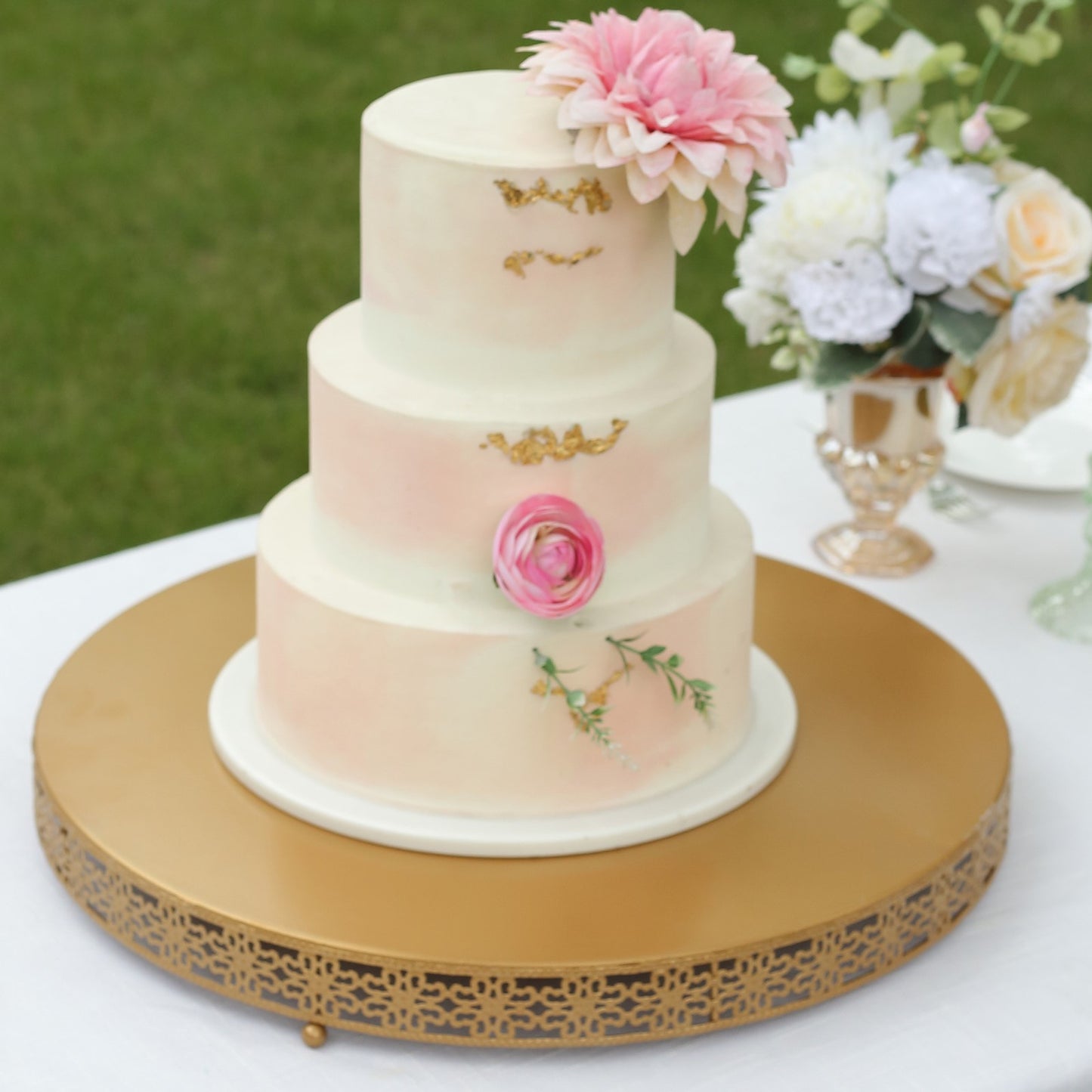Gold metal Fleur De Lis pedestal cake stand with a three-tiered cake centerpiece.