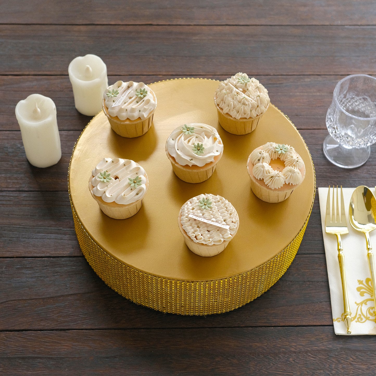 Gold round metal pedestal cake stand with cupcakes on a wooden table.