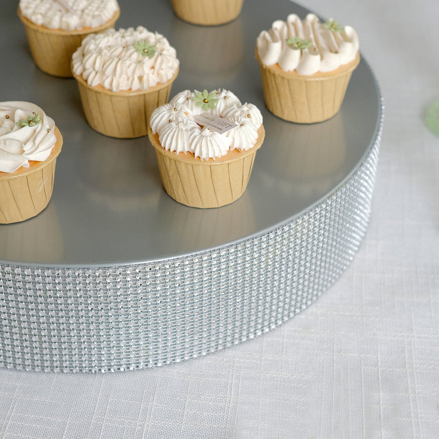 Silver rhinestone round metal cake stand with cupcakes on top.