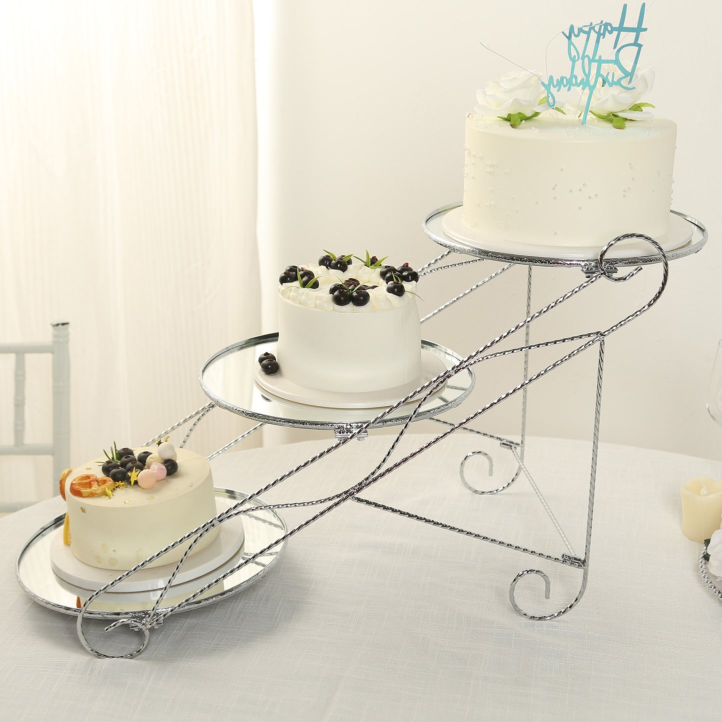 Silver 3-tier cupcake stand with mirror trays, displaying three decorated cakes.