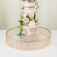Gold metal cake stand with glass top, ornate round dessert display tray.