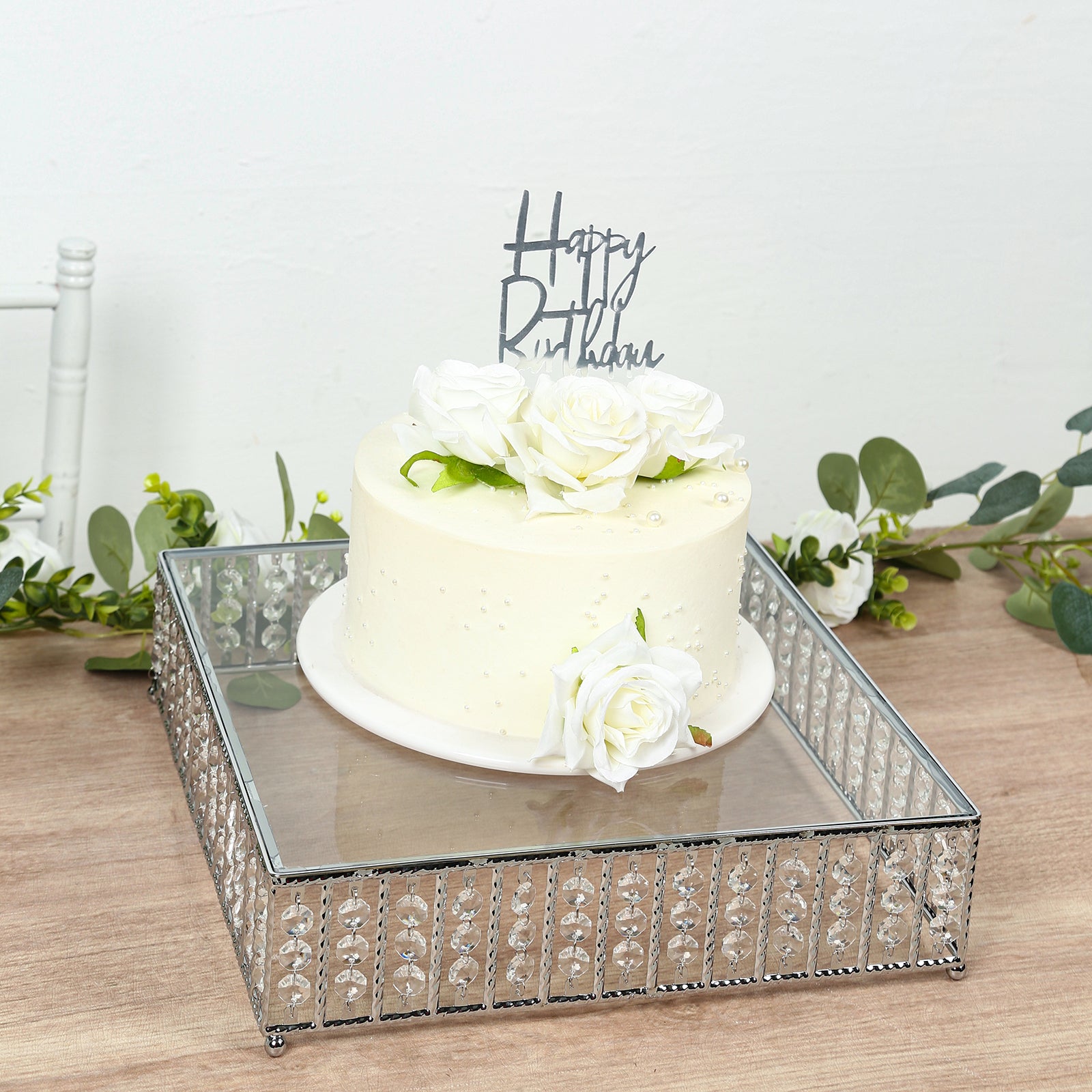 Silver cake stand with hanging crystal beads and glass top, displaying a white cake.