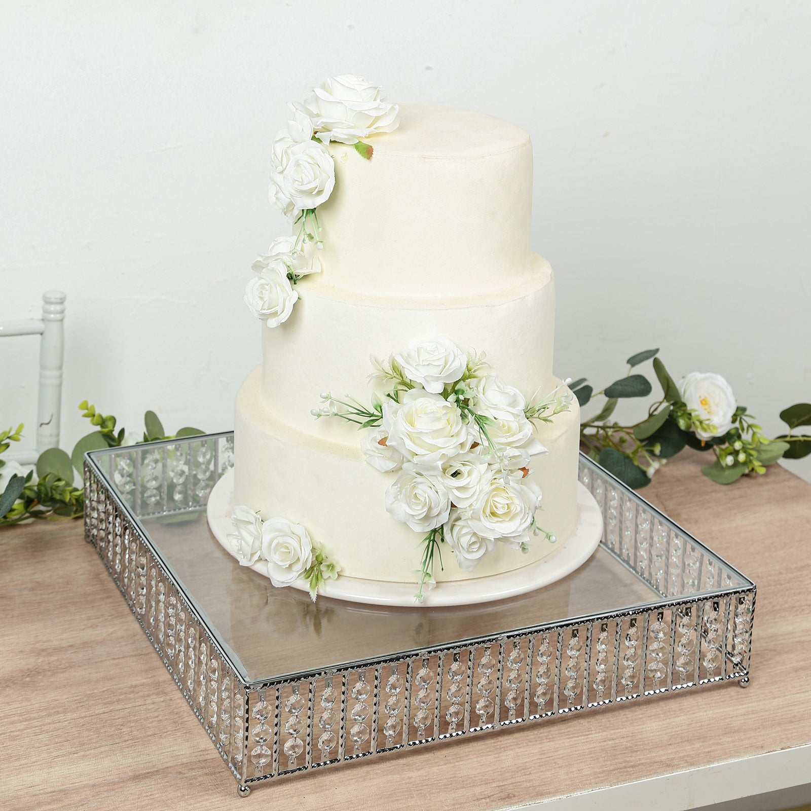 Silver cake stand with hanging crystal beads, displaying a white floral cake.