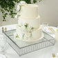 Silver cake stand with hanging crystal beads and glass top displaying a white cake.