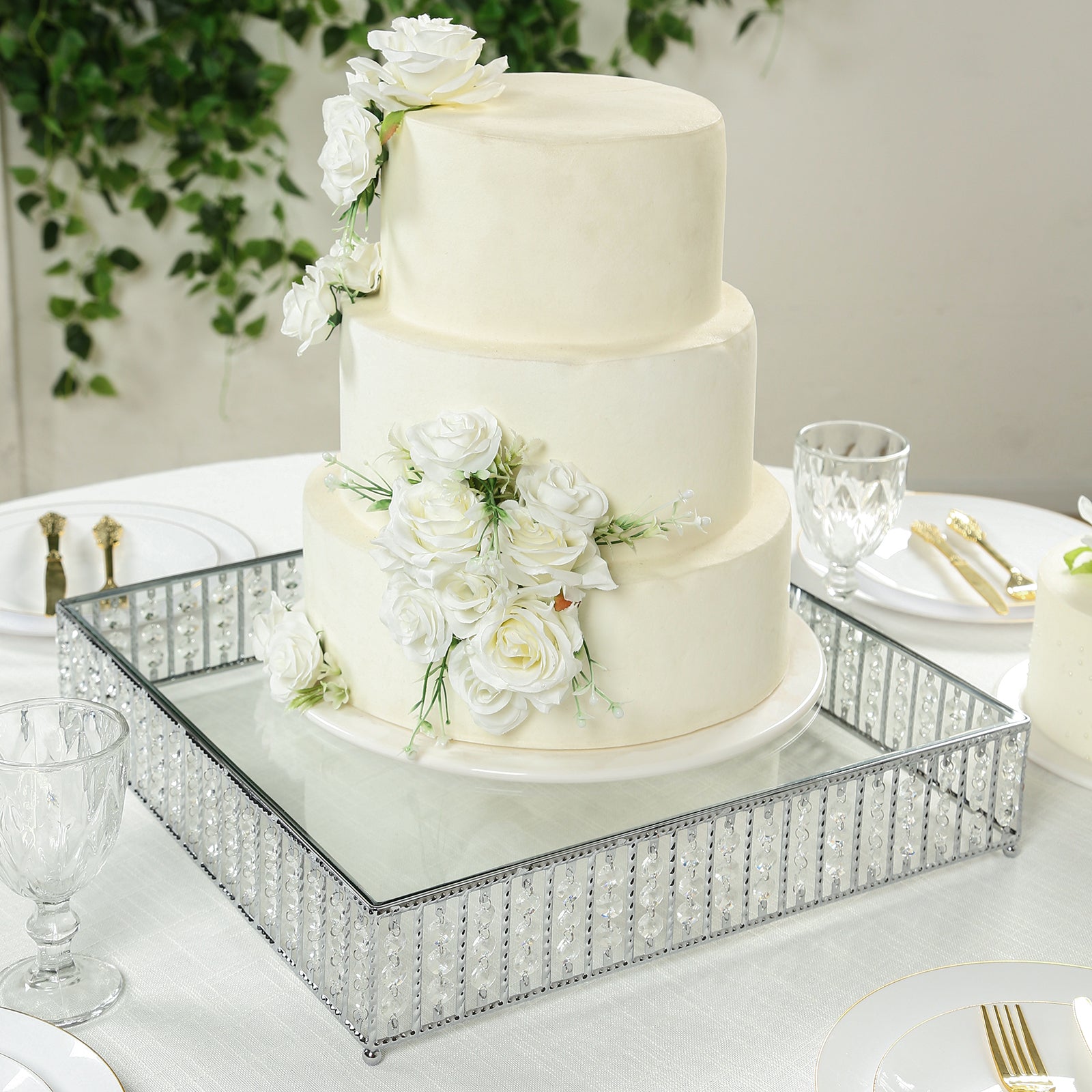 Silver cake stand with hanging crystal beads and glass top displaying a white cake.