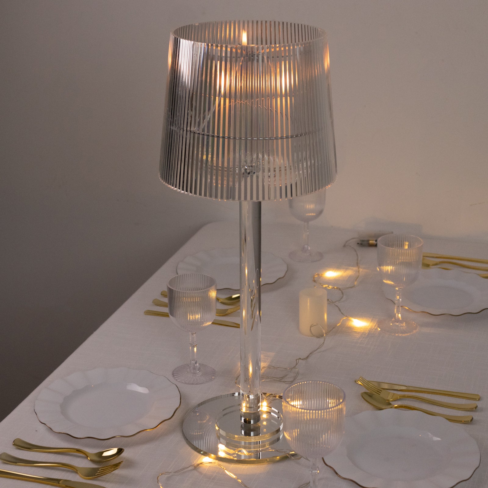 Clear acrylic ribbed candle lamp on a table setting with gold accents.