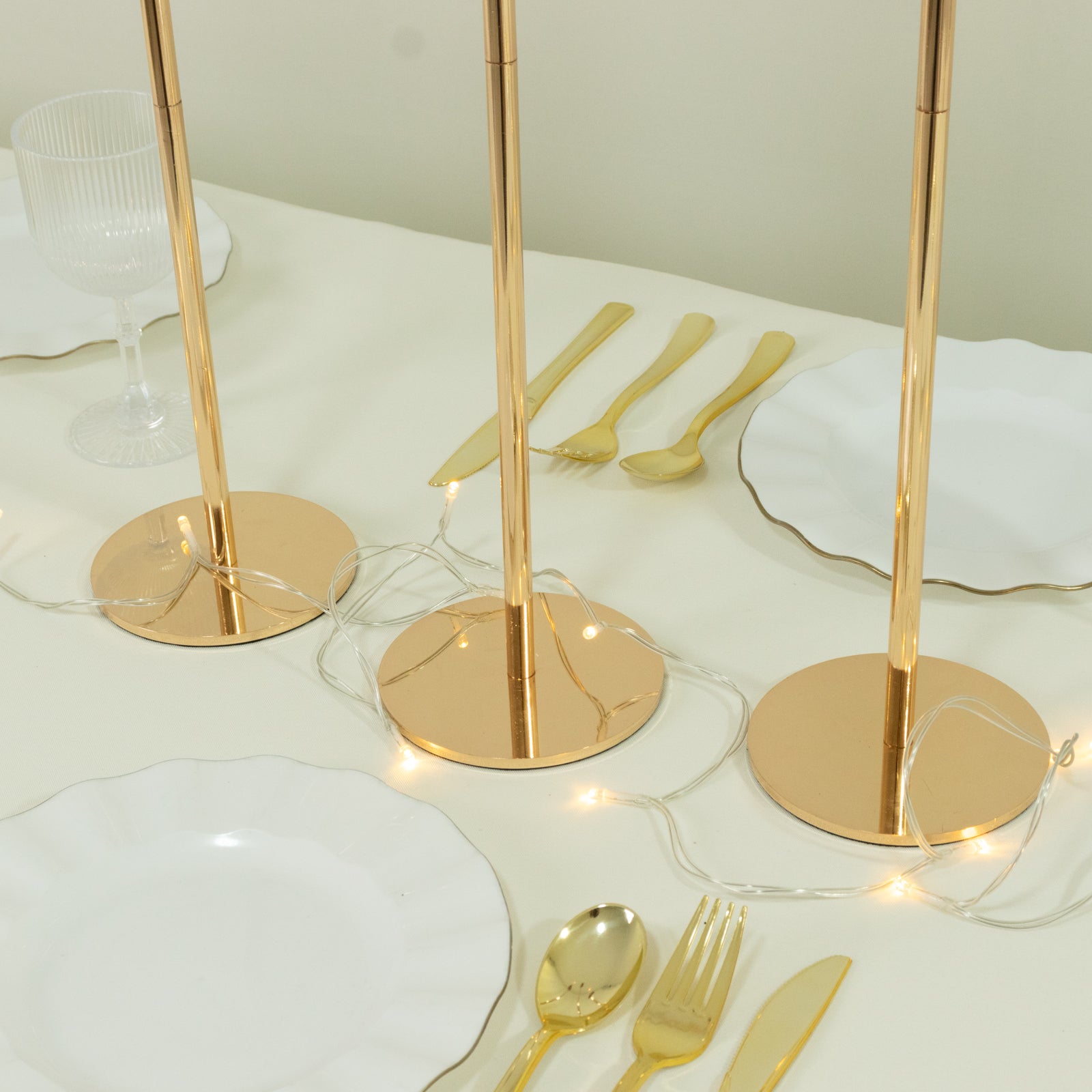 Gold metal taper candle holders with hurricane glass shades on a table setting.