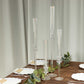 Clear acrylic hurricane candle stands in four heights on a wooden table.