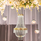 Gold beaded crystal chandelier with ornate metal frame and floral backdrop.
