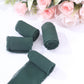 Hunter emerald green chiffon ribbon rolls on a white surface with pink roses in the background.