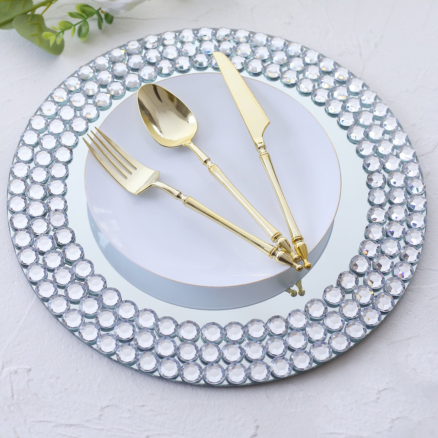 Silver mirror glass charger plate with diamond beaded rim and gold utensils.