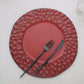 Burgundy hammered charger plate with black utensils on a light surface.