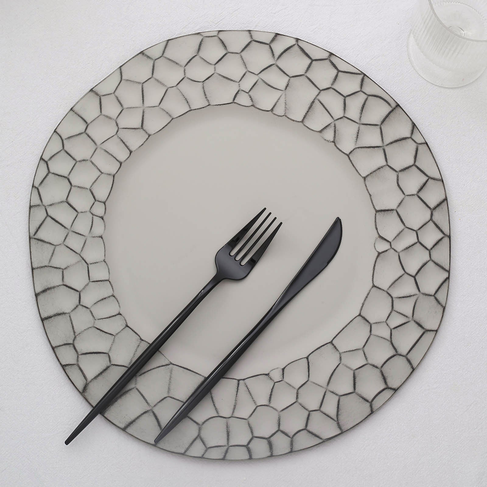Matte finish gray hammered charger plate with black utensils.