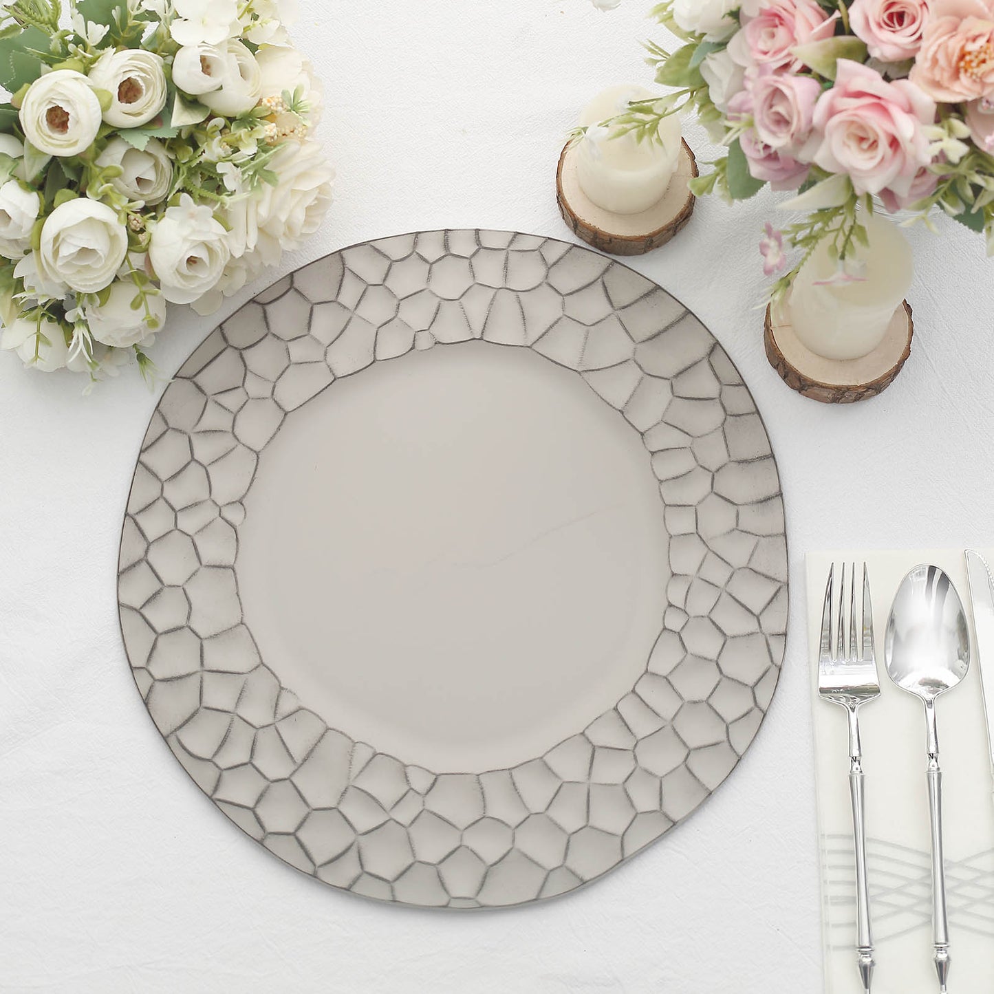 Matte finish gray hammered charger plate on a table with flowers and utensils.