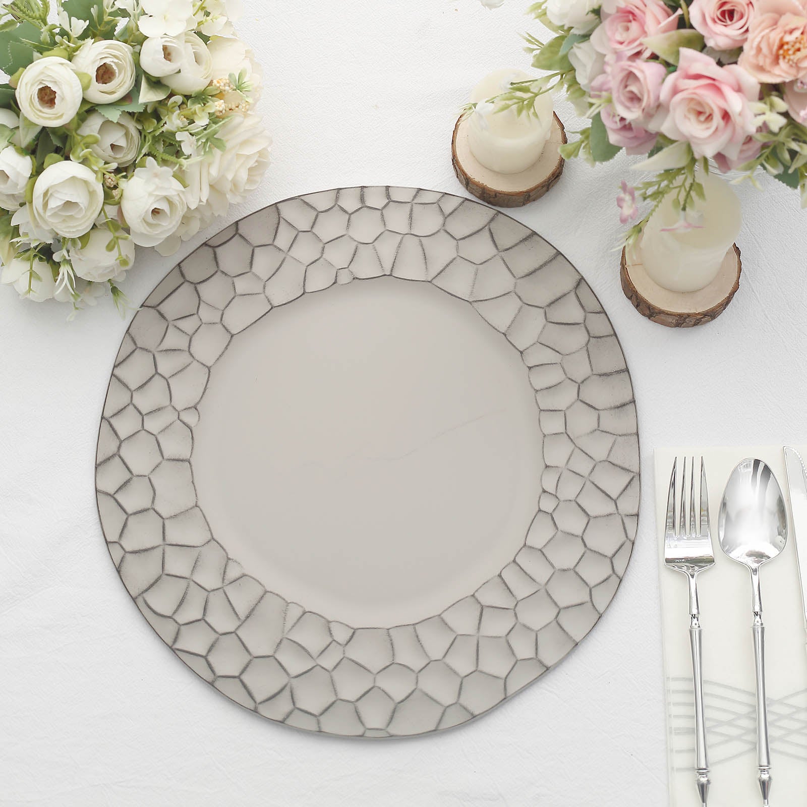 Matte finish gray hammered charger plate on a table with flowers and utensils.