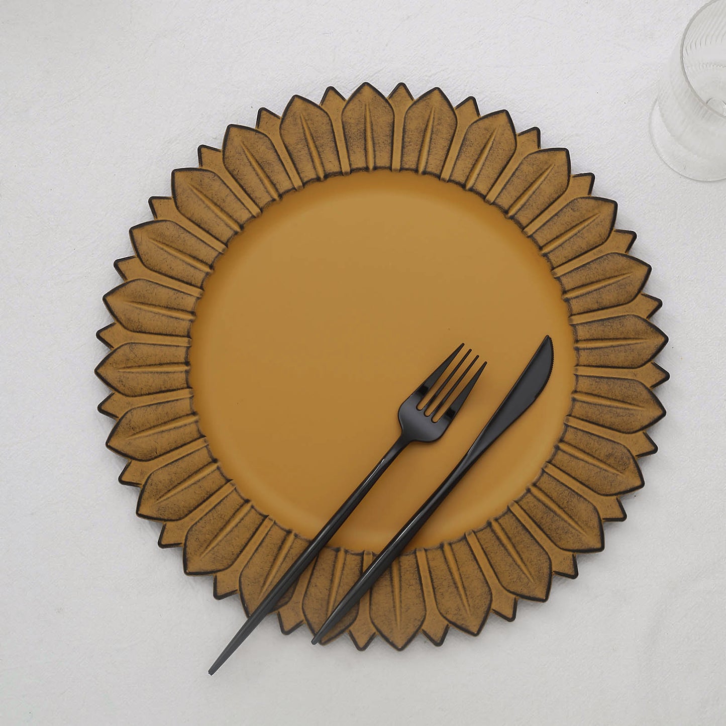 Matte mustard yellow sunflower charger plate with black utensils.