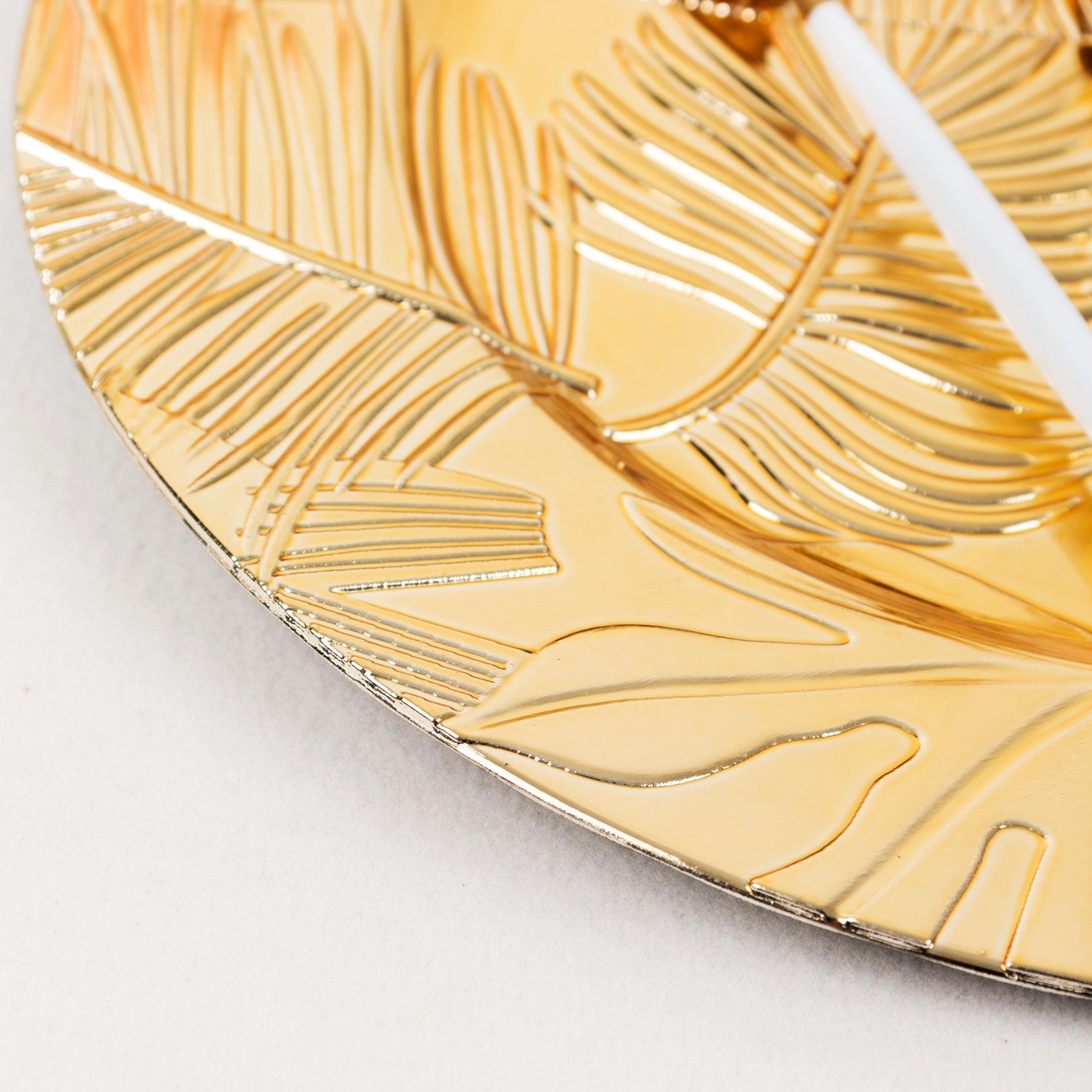 Metallic gold acrylic charger plate with embossed tropical leaves design.