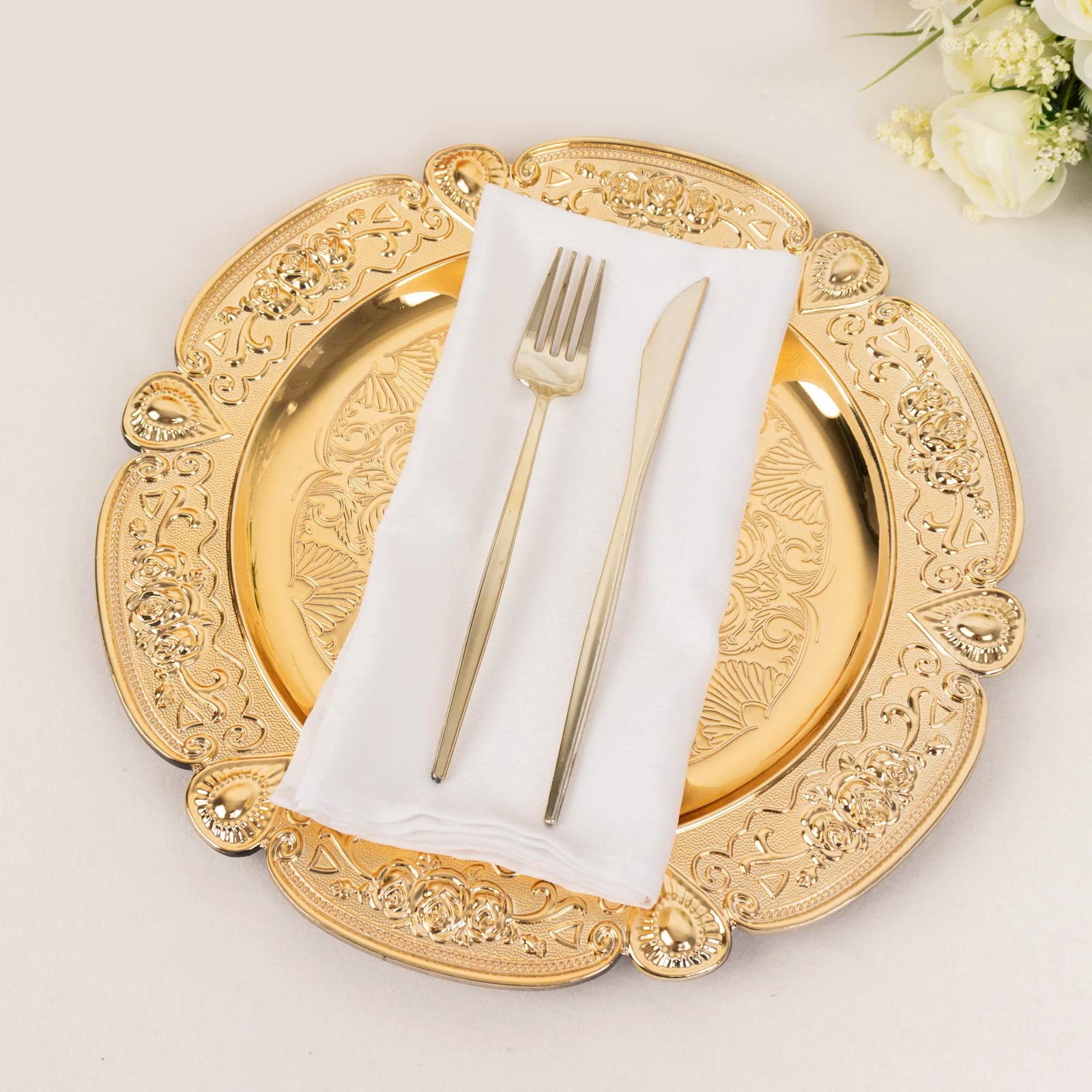 Gold floral embossed charger plate with scalloped rim and silver utensils.