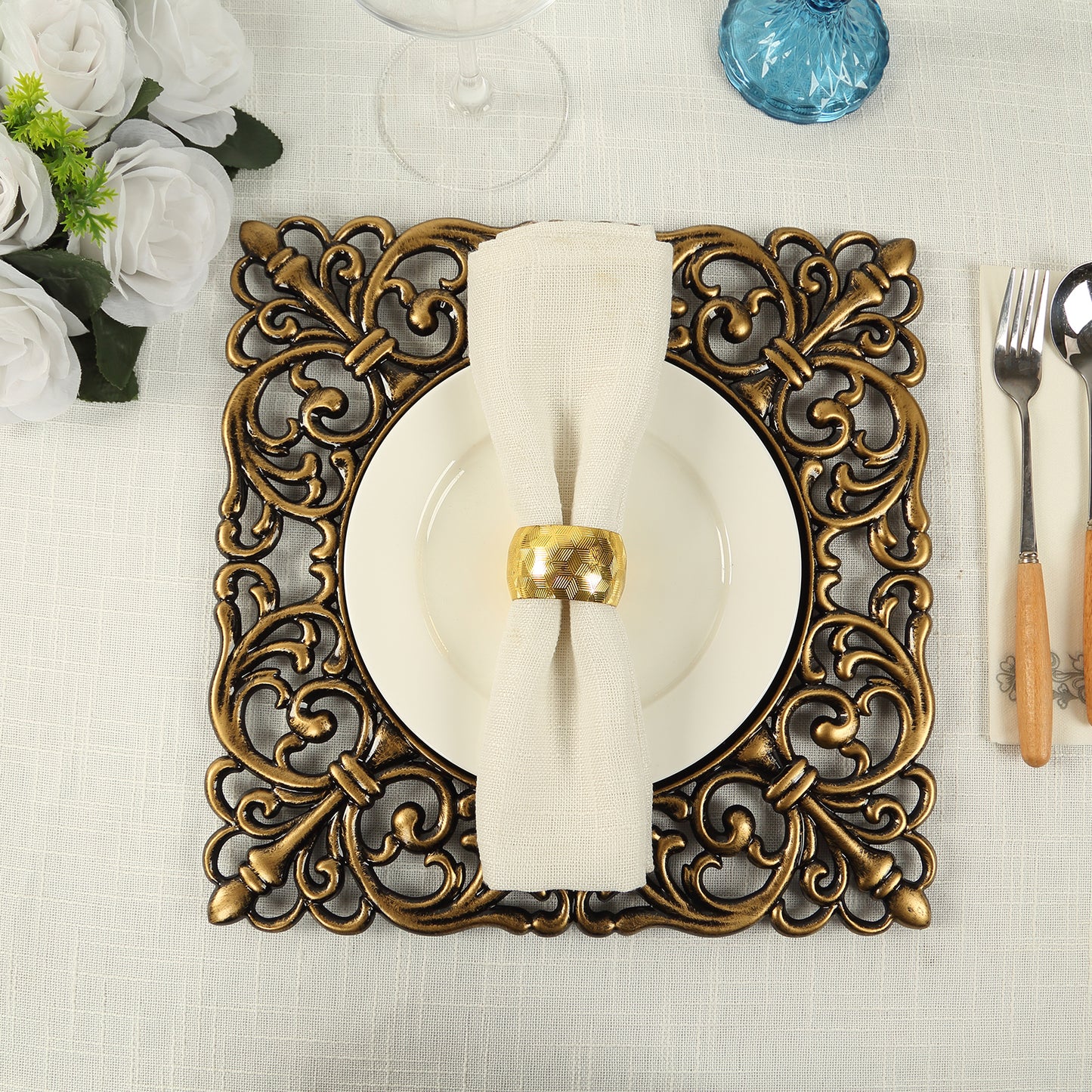 Black square acrylic charger plate with antique gold lace border on a table setting.
