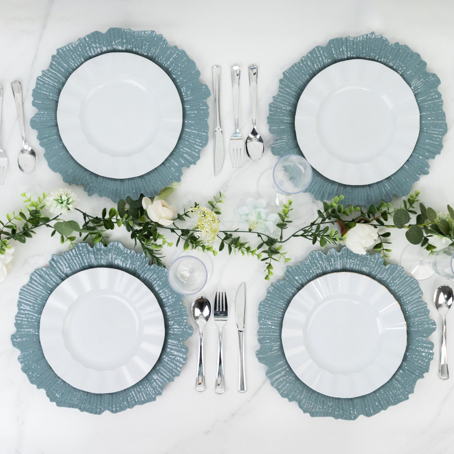 Dusty blue charger plates arranged on a table with silver utensils and greenery.