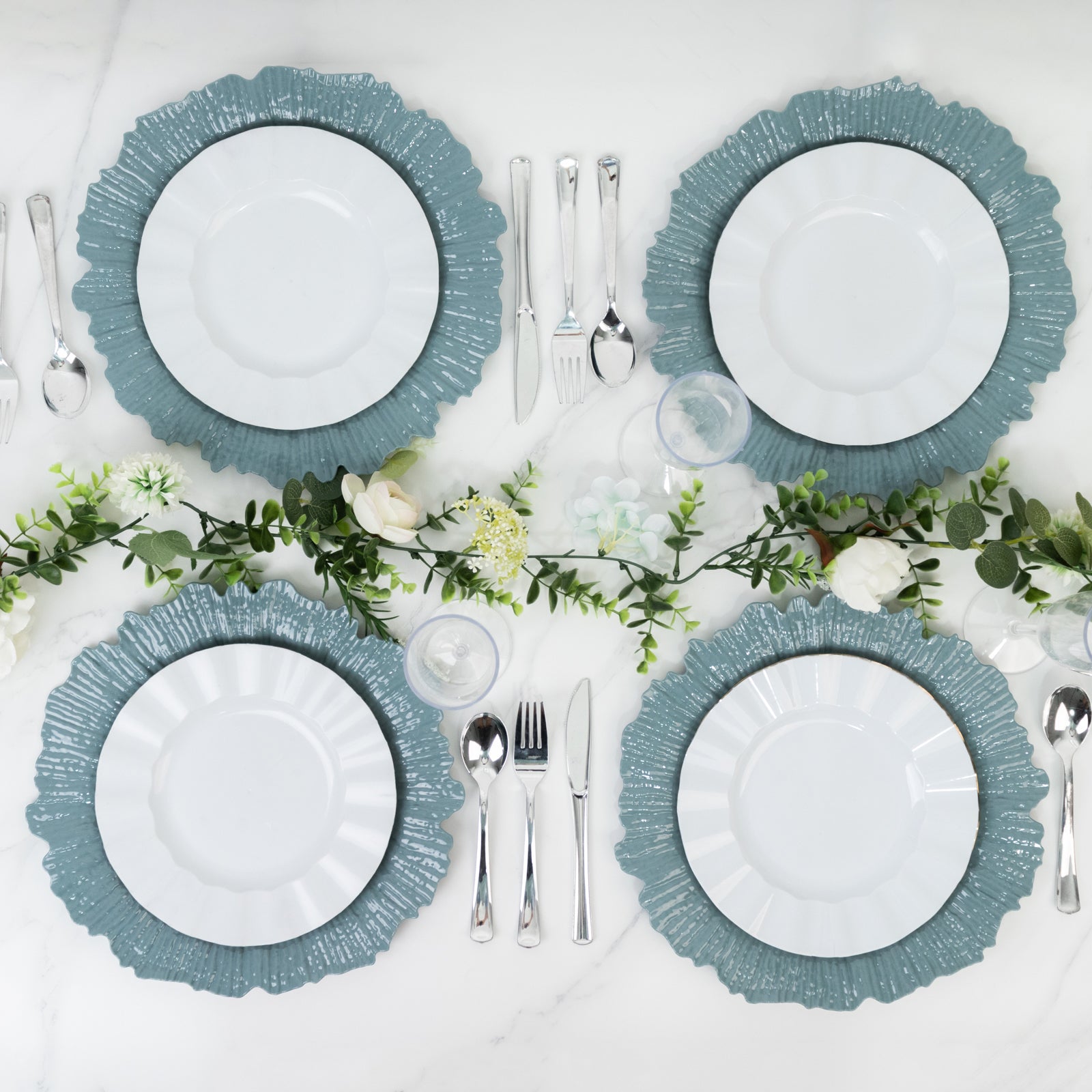 Dusty blue charger plates arranged on a table with silver utensils and greenery.