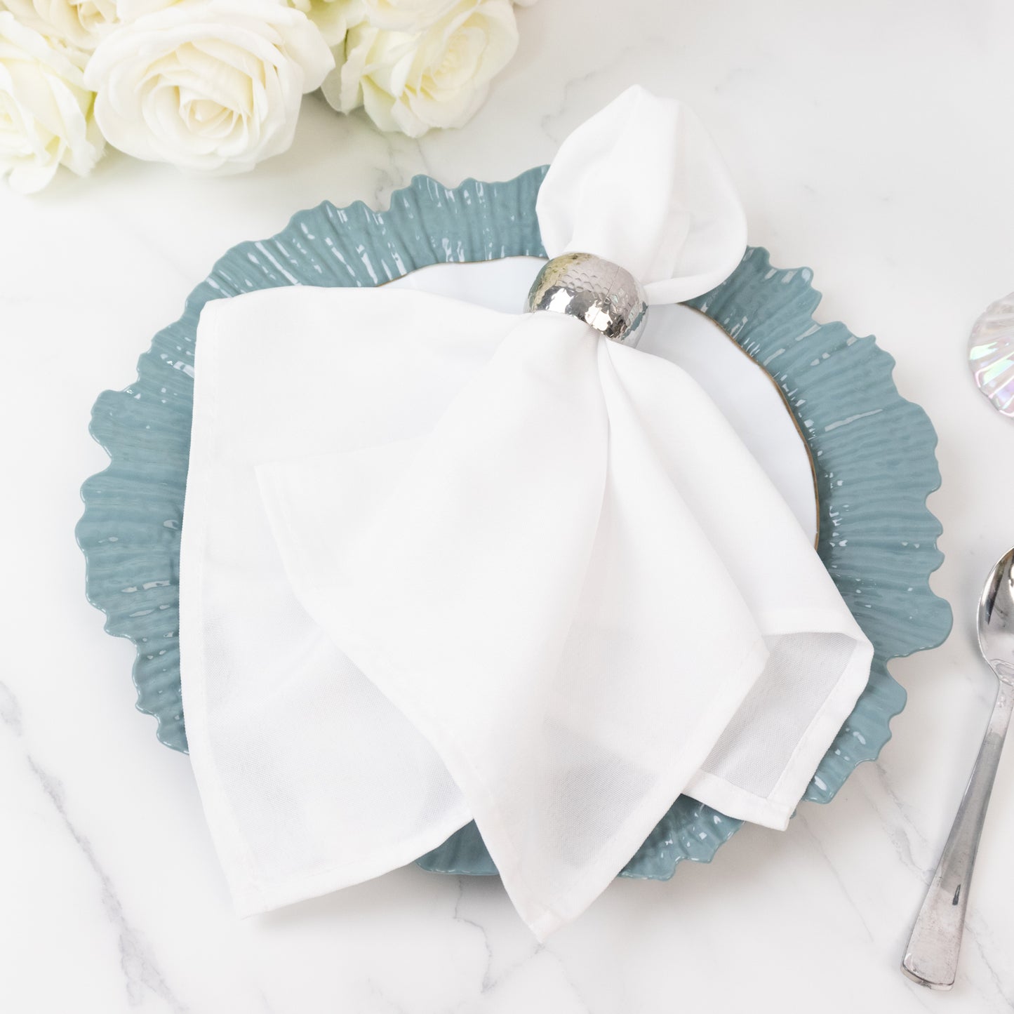 Dusty blue charger plate with white napkin and silver napkin ring on a marble table.