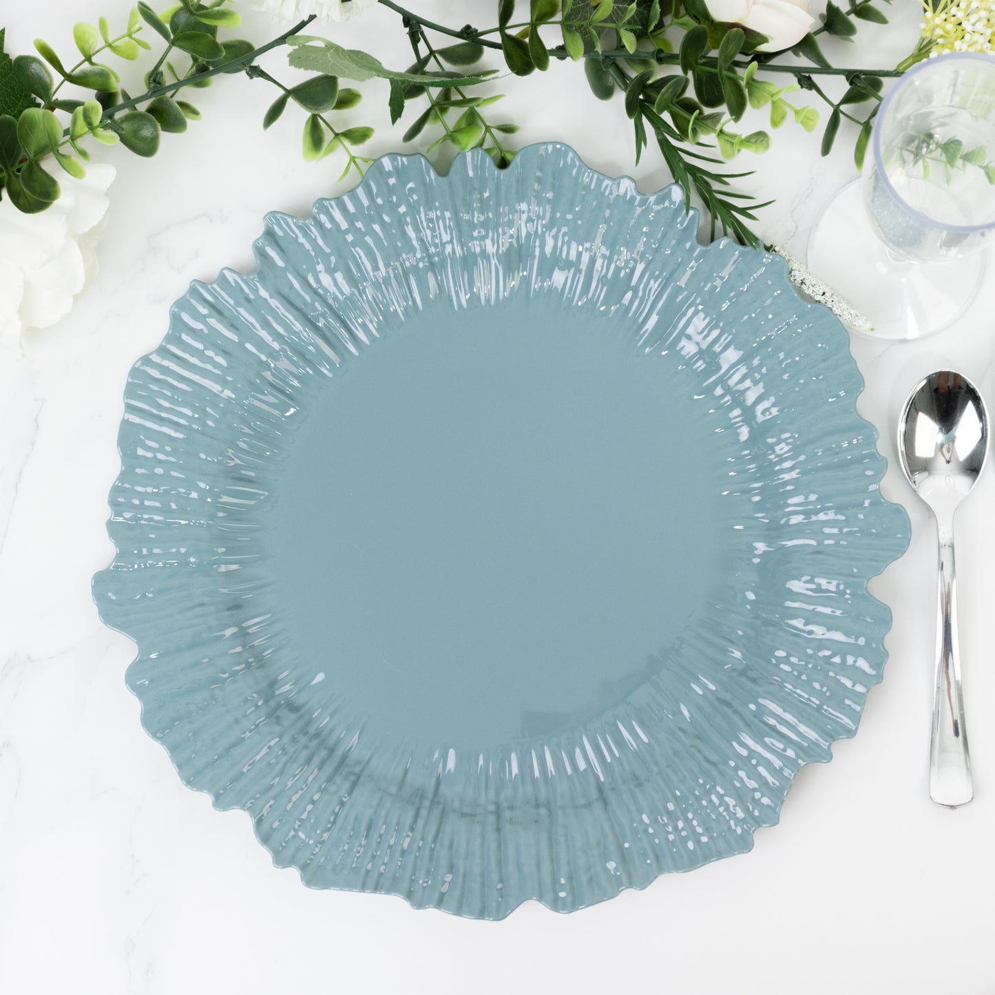 Dusty blue plastic charger plate with a scalloped edge on a table setting.