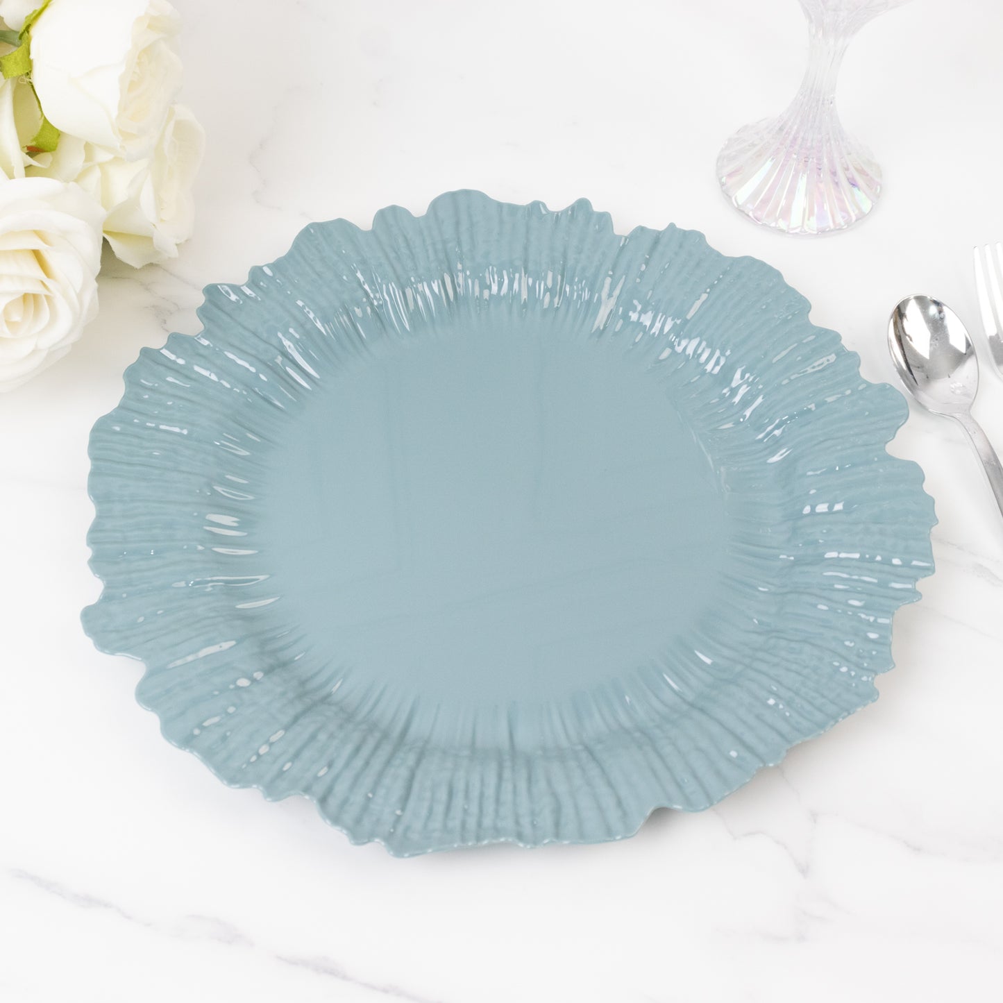 Dusty blue plastic charger plate with a ruffled edge on a marble surface.