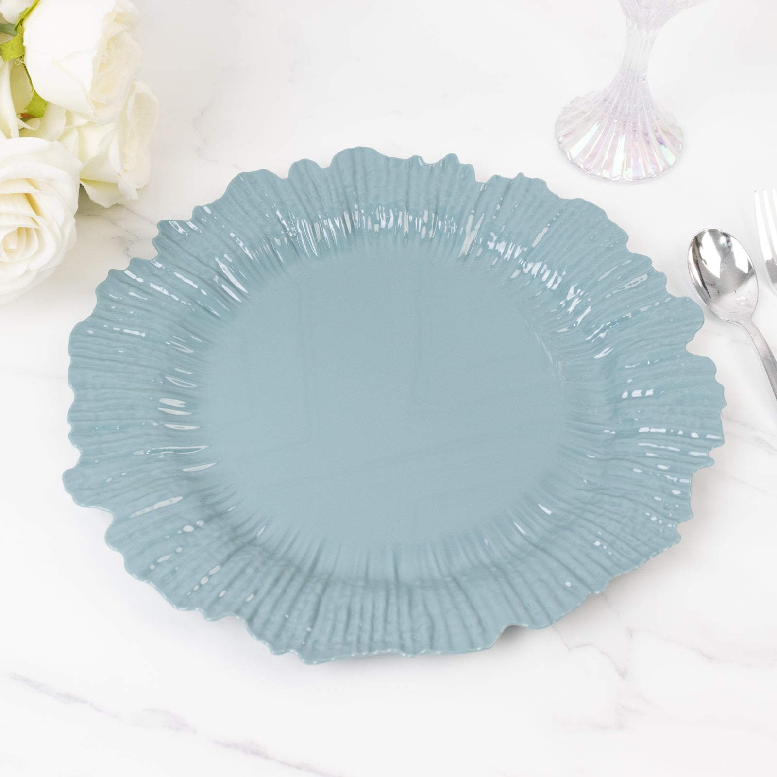 Dusty blue plastic charger plate with a ruffled edge on a marble surface.