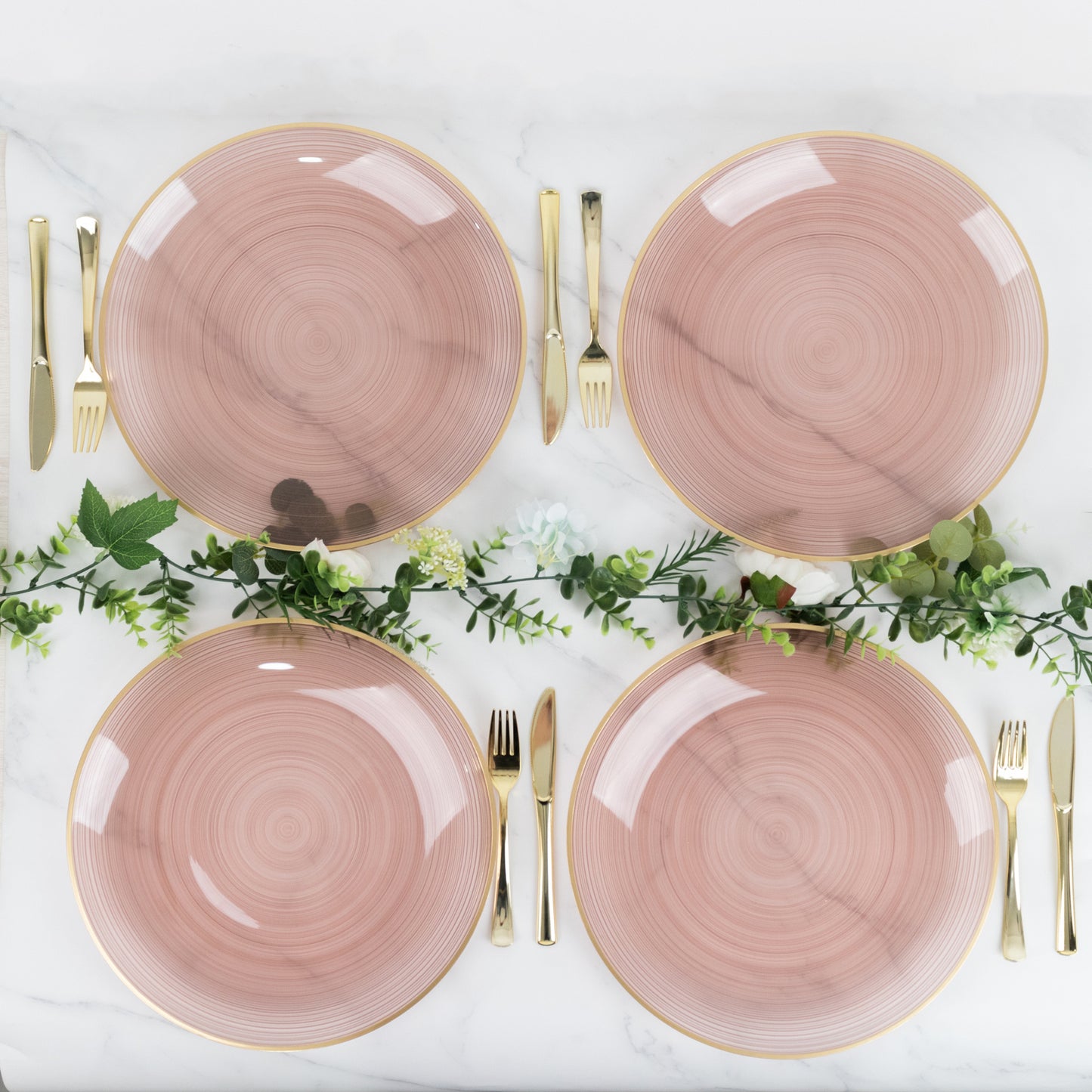 Transparent dusty rose swirl charger plates with gold rim on a marble table setting.