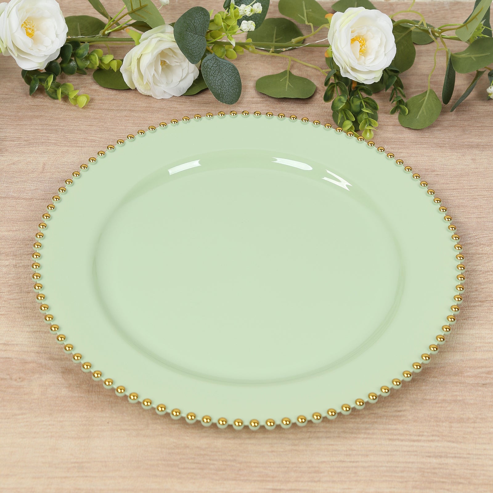 Sage green charger plate with gold beaded rim on a wooden table.