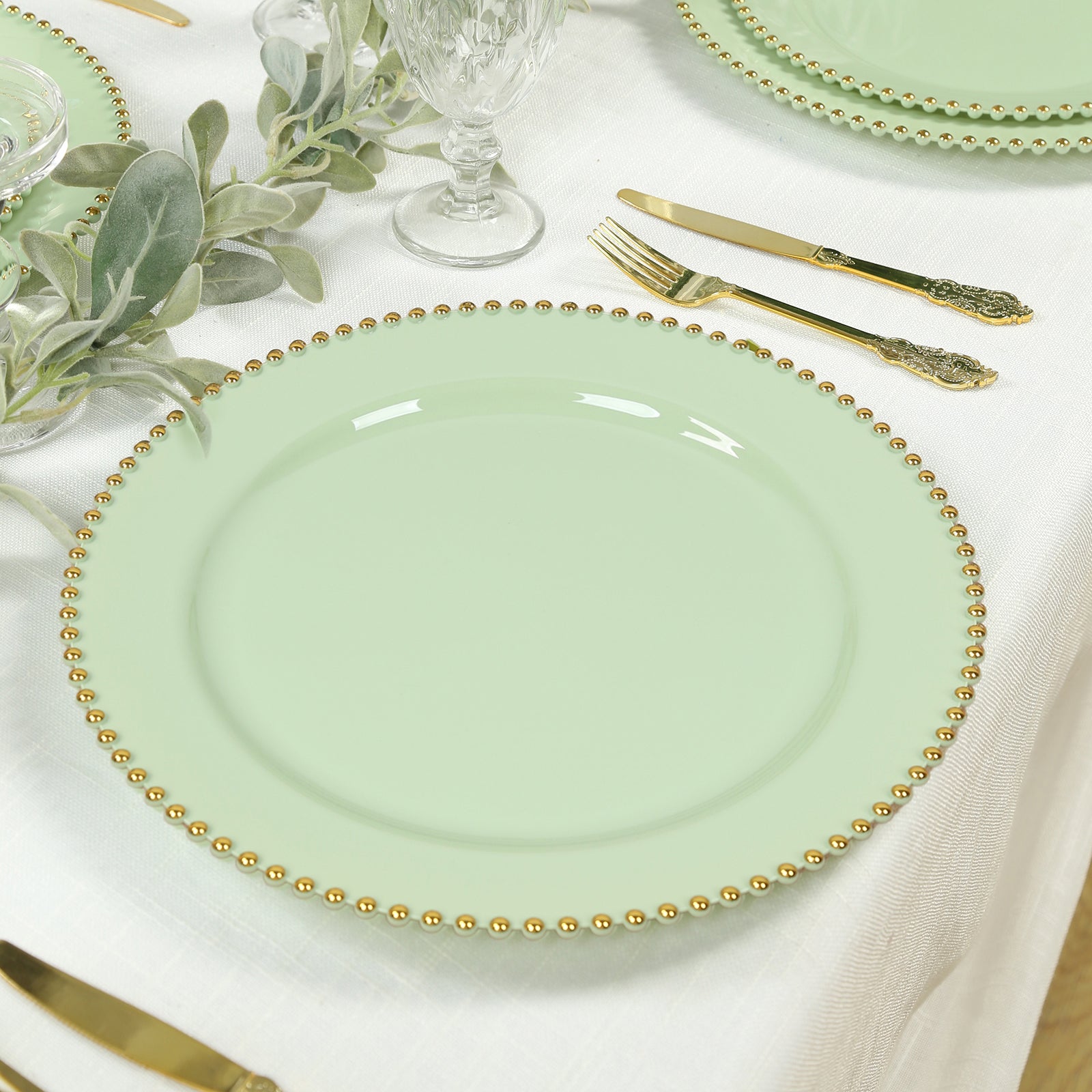 Sage green charger plate with gold beaded rim on a dining table.