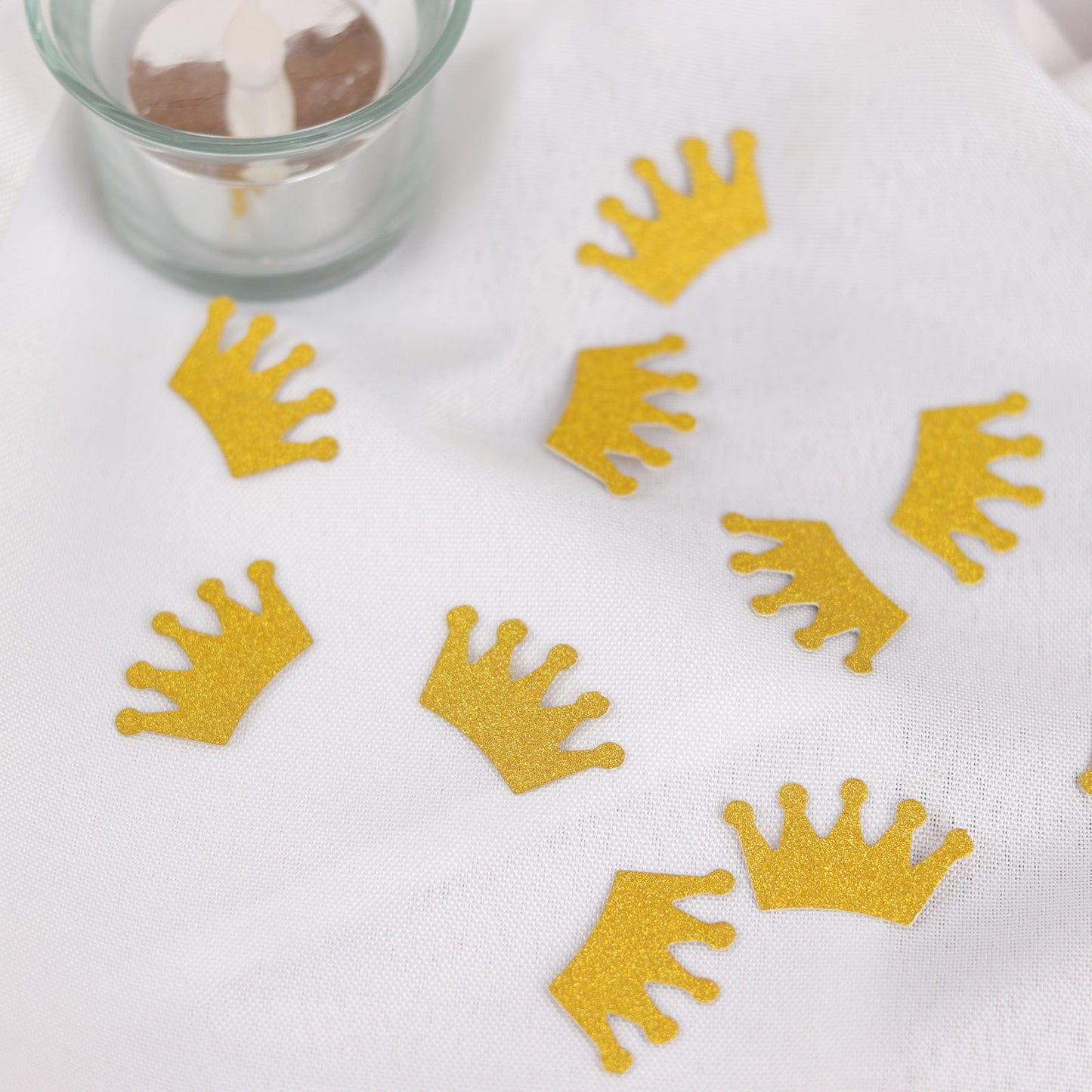 Gold glitter crown confetti scattered on a white surface.
