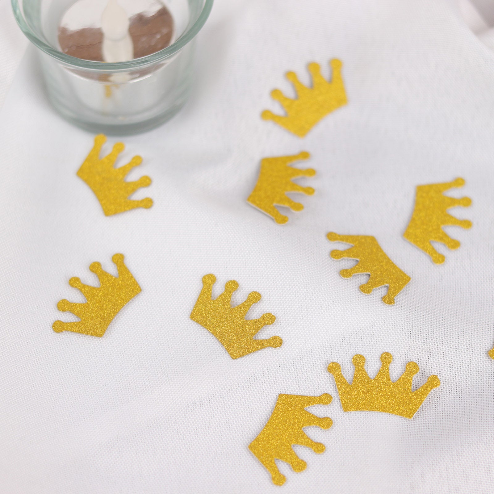 Gold glitter crown confetti scattered on a white surface.