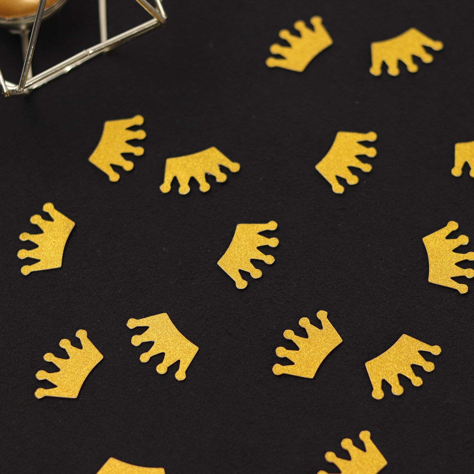 Gold glitter crown paper confetti scatters on a black surface.