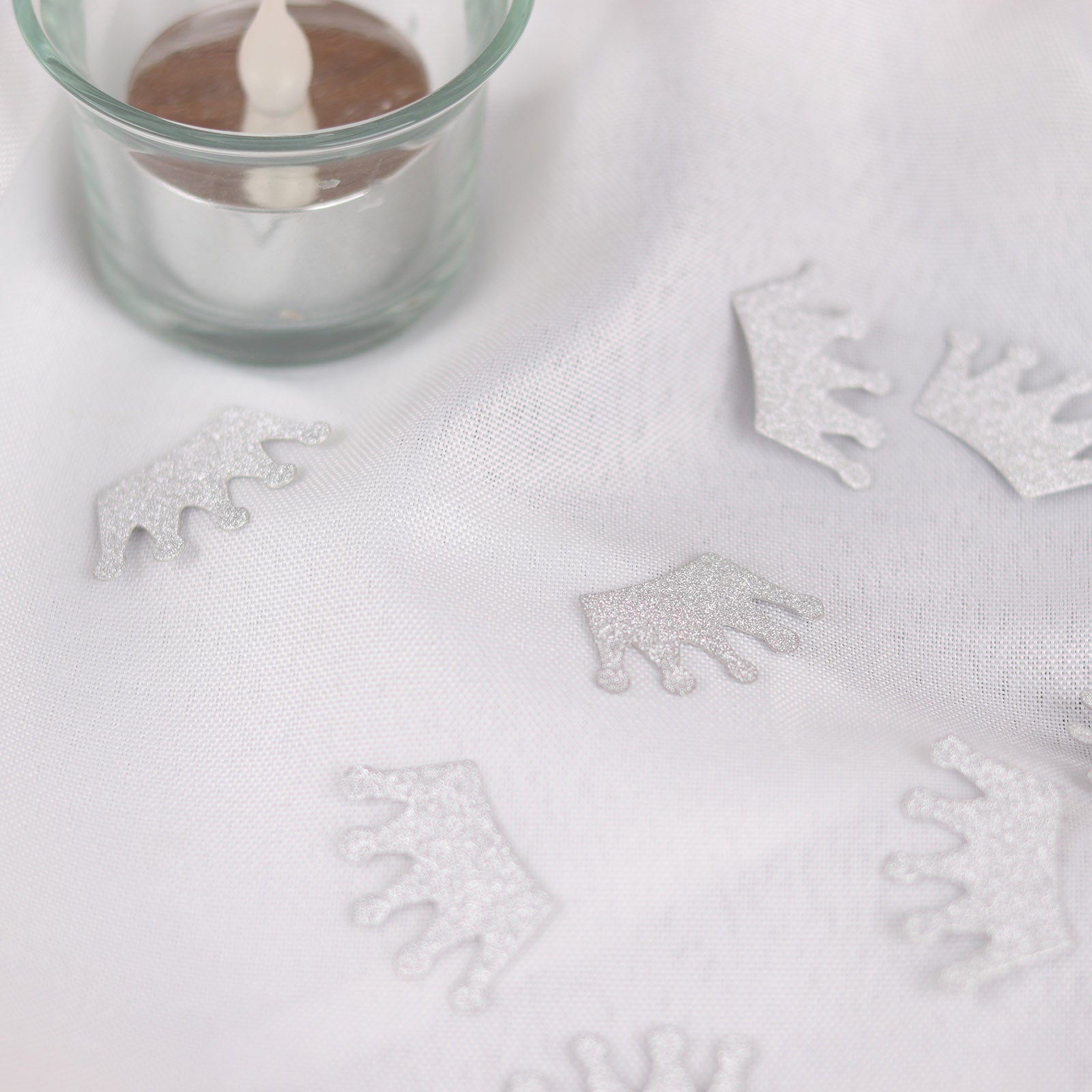 Silver glitter crown confetti on a white tablecloth for party decoration.