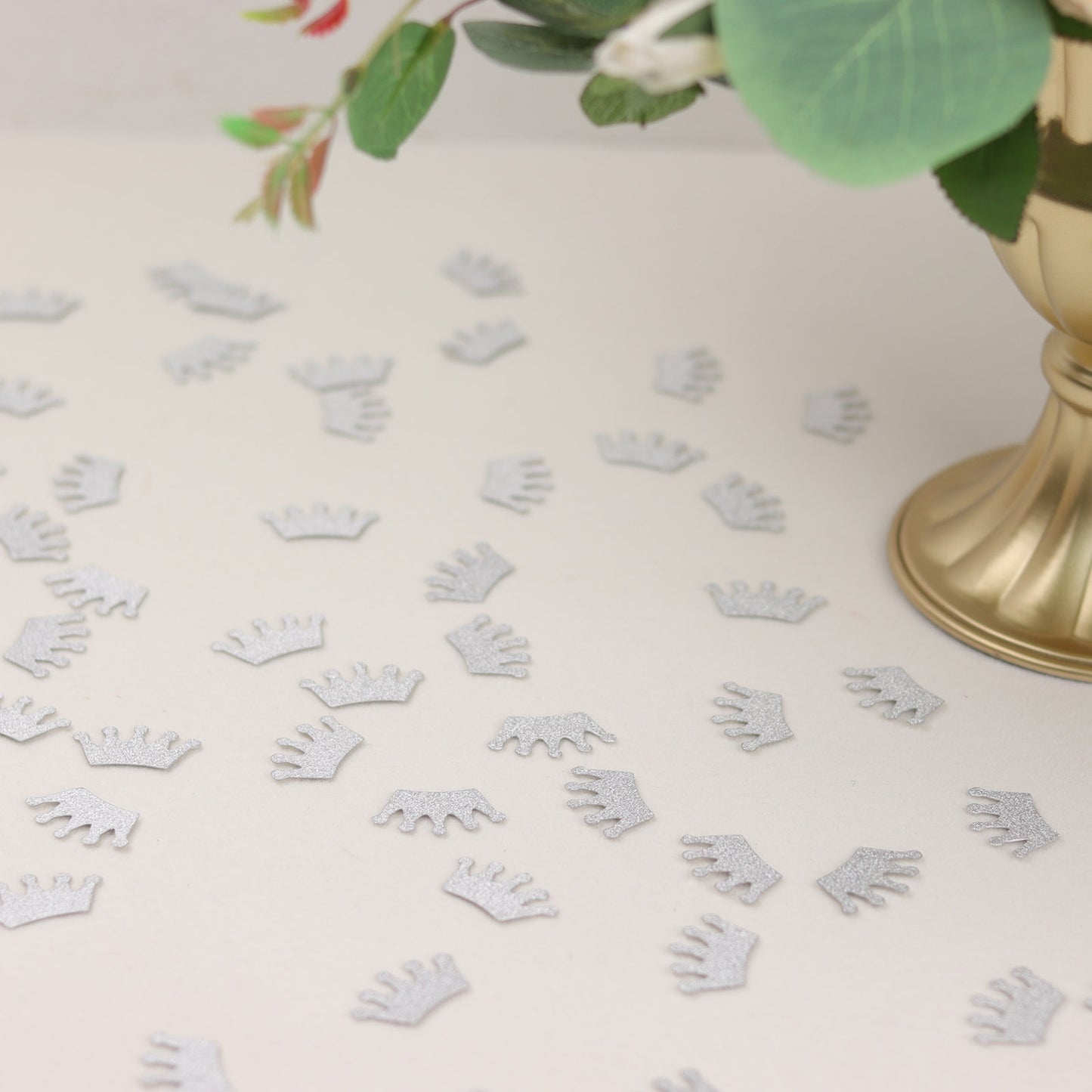 Silver glitter crown confetti scattered on a table for a princess theme party.