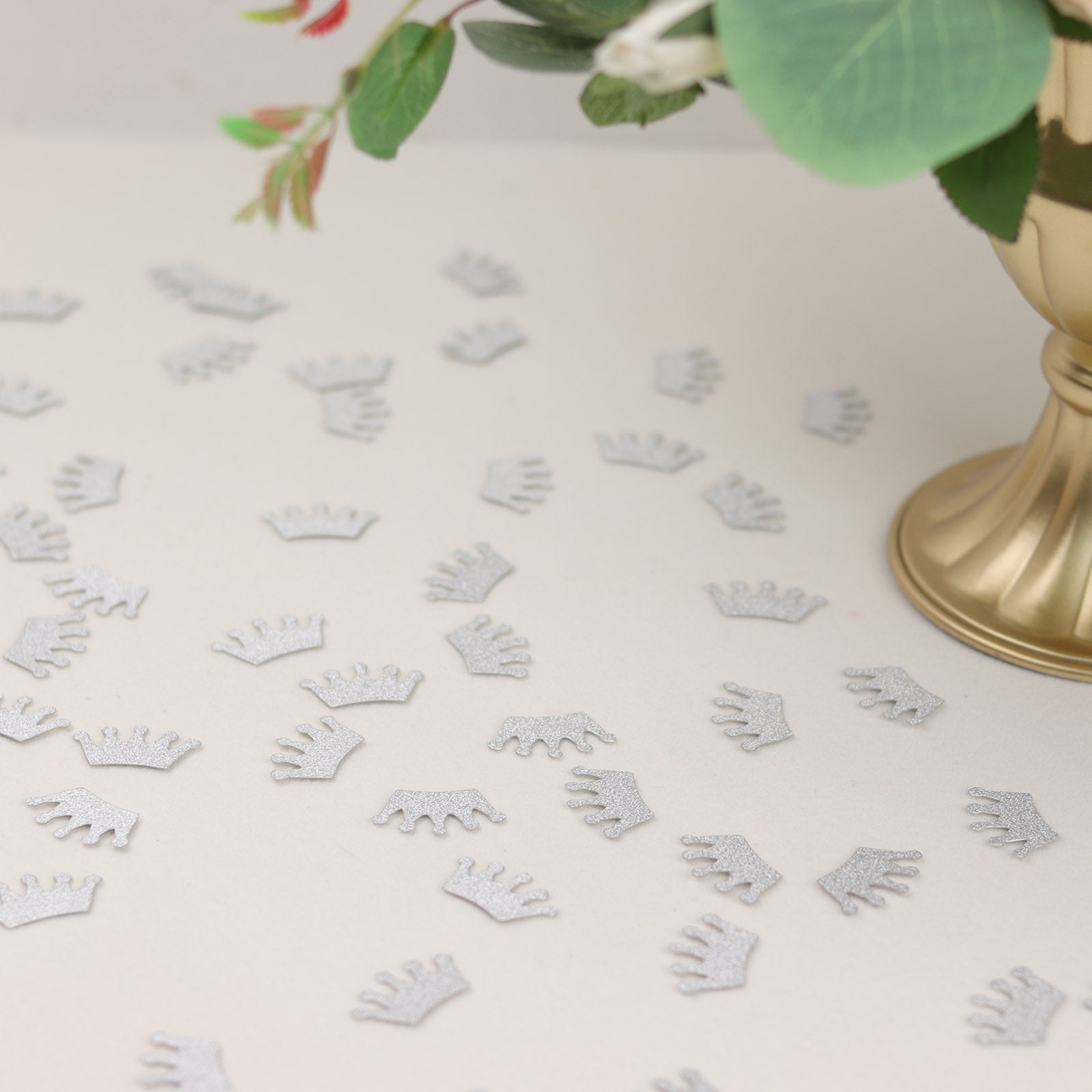 Silver glitter crown confetti scattered on a table for a princess theme party.