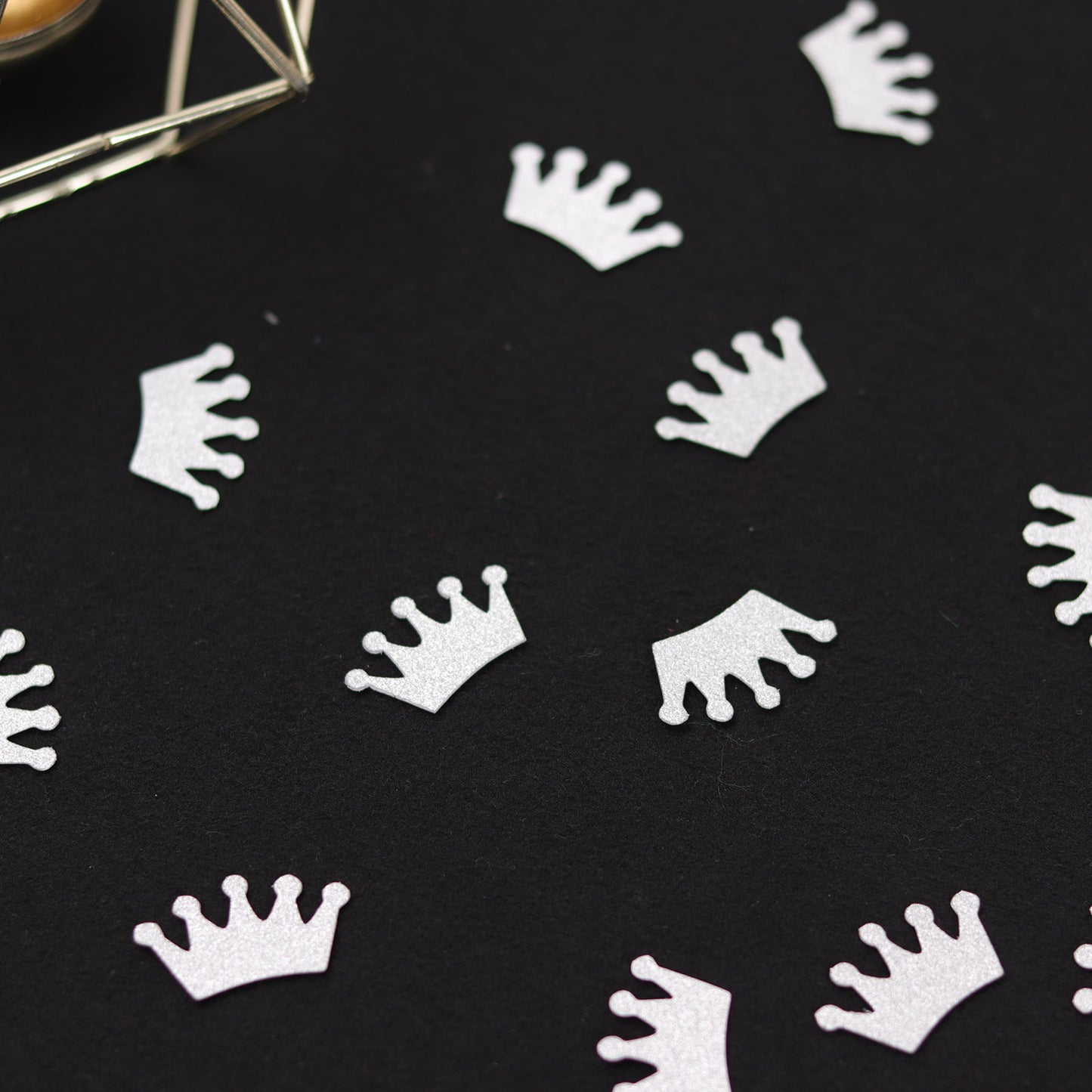 Silver glitter crown confetti on a dark background for party decoration.