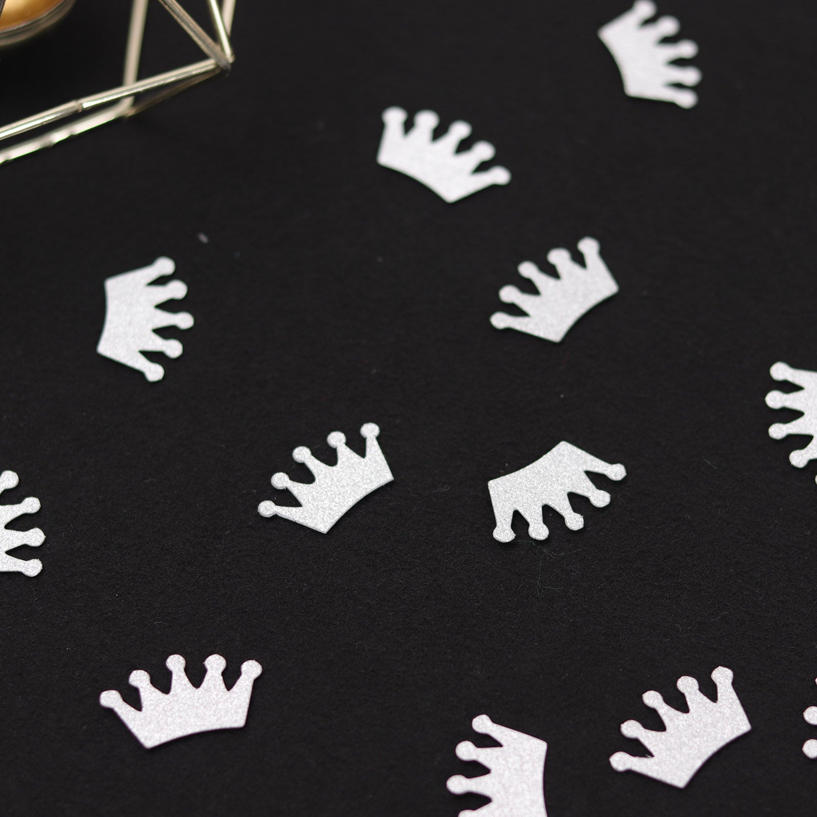 Silver glitter crown confetti on a dark background for party decoration.