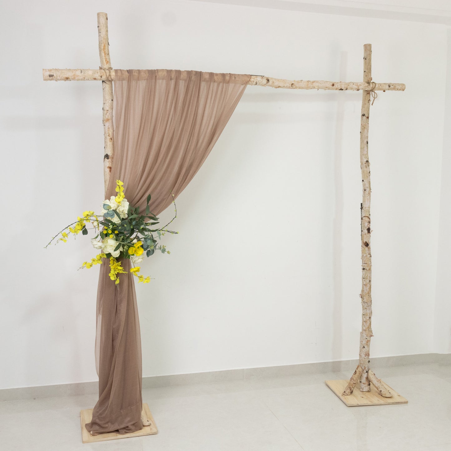Taupe sheer backdrop drape on a wedding arch with floral arrangement.