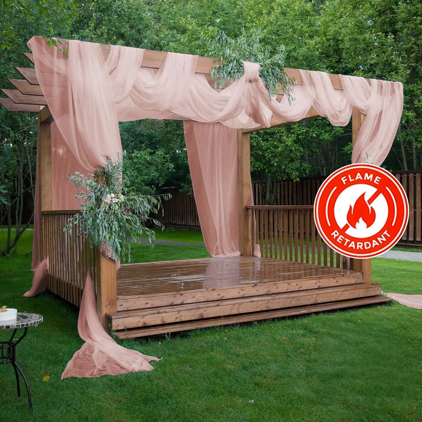 Dusty rose chiffon curtain panel draping a wooden pergola in a garden setting.