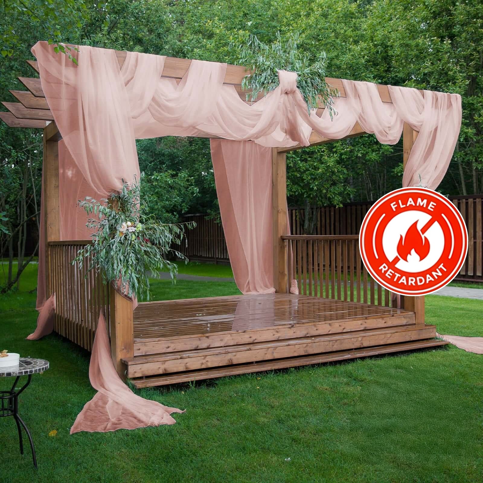 Dusty rose chiffon curtain panel draping a wooden pergola in a garden setting.