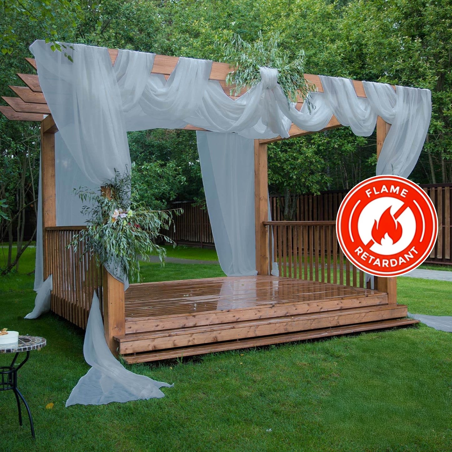 Dusty blue chiffon curtain panel draping a wooden pergola in a garden setting.