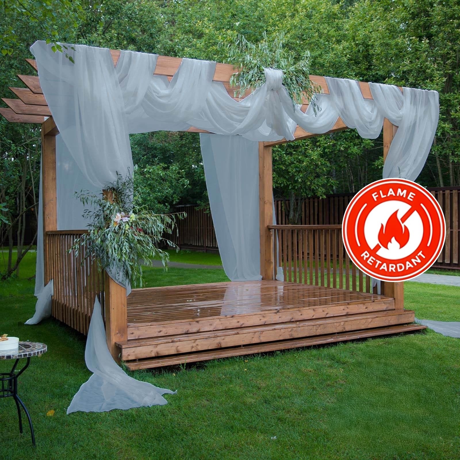 Dusty blue chiffon curtain panel draping a wooden pergola in a garden setting.