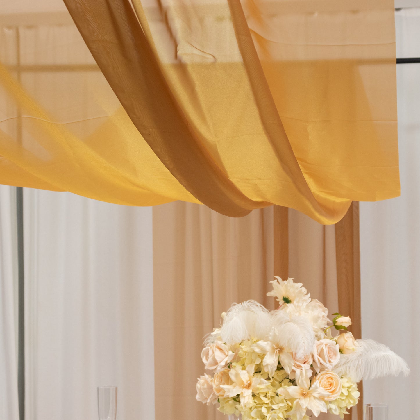 Gold chiffon curtain panel elegantly draped above floral arrangement.