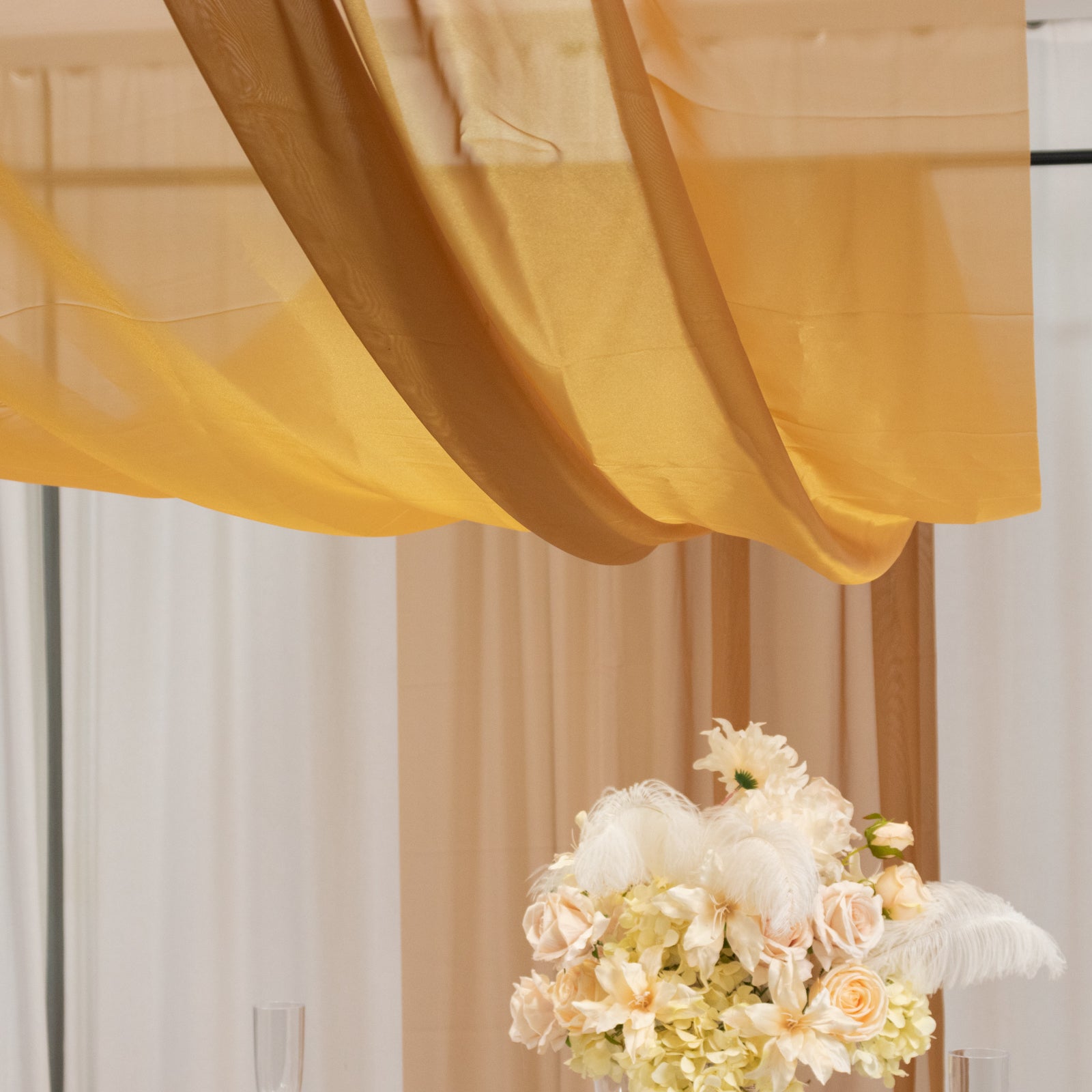 Gold chiffon curtain panel elegantly draped above floral arrangement.