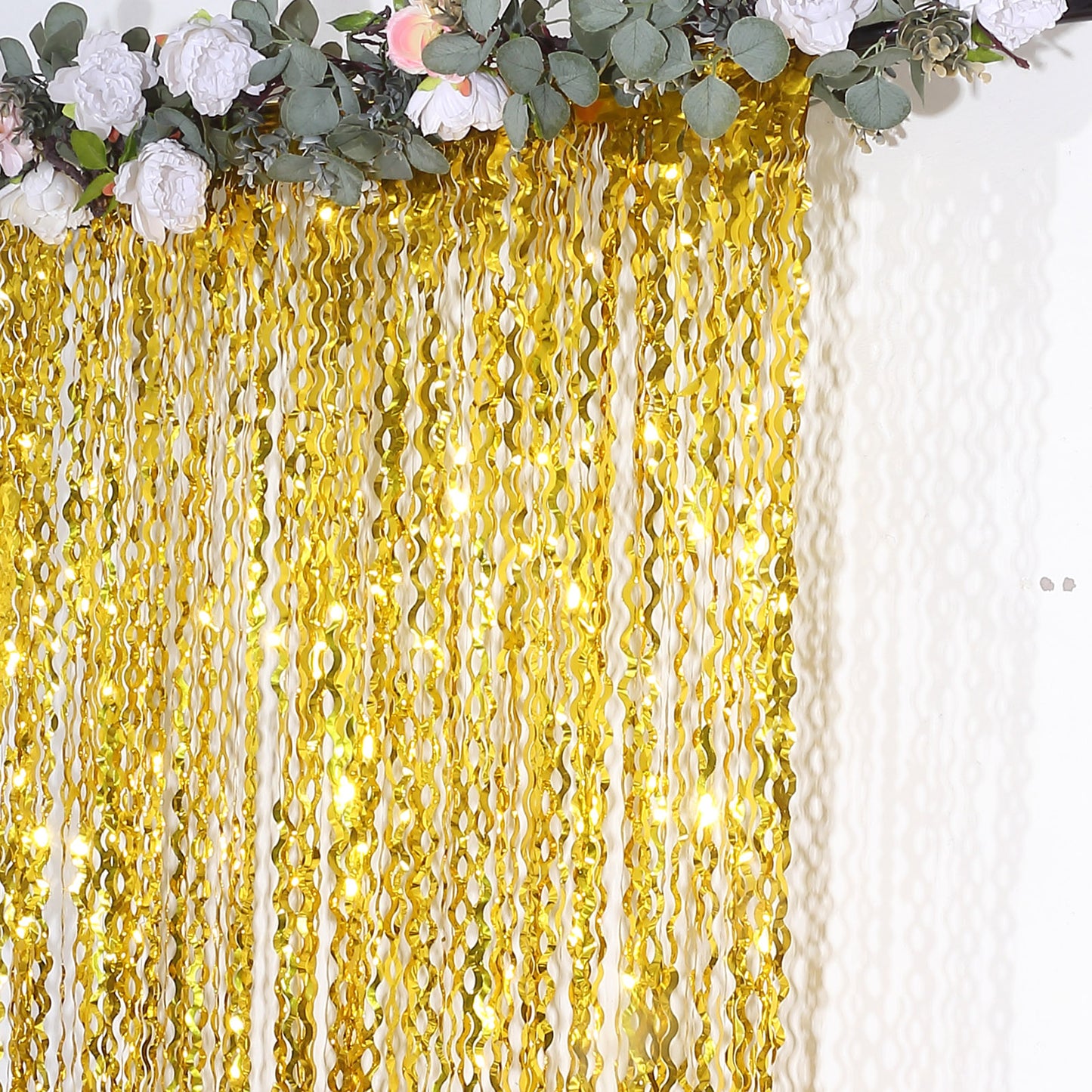 Metallic gold wavy foil fringe party backdrop with curly tinsel streamers.