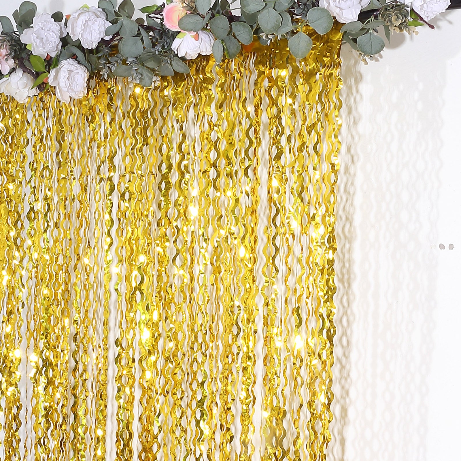 Metallic gold wavy foil fringe party backdrop with curly tinsel streamers.