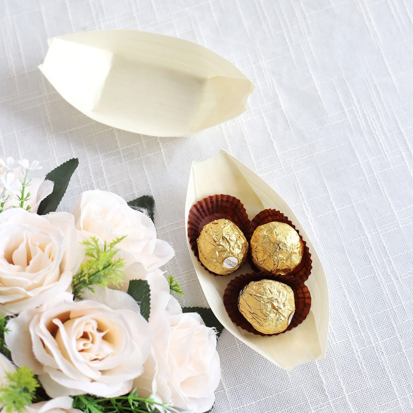 Natural biodegradable wooden boat-shaped food plates with gold-wrapped snacks.